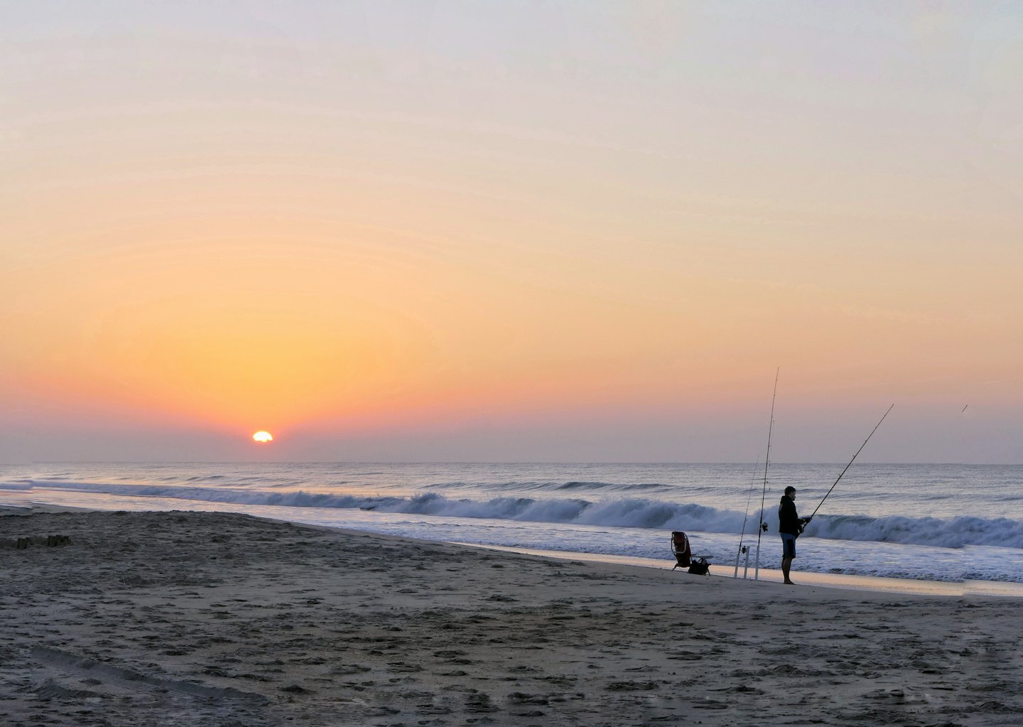 Wędkarze na plaży o wschodzie słońca z falami rozbijającymi się o brzeg.